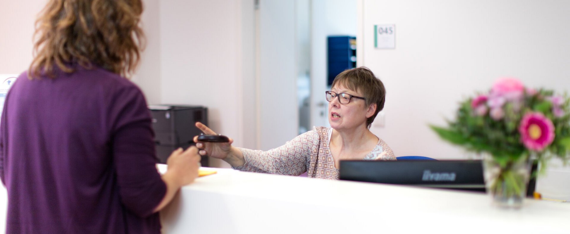 Patientin im Gespräch mit Mitarbeiterin der Tropenambulanz an Empfangstheke.