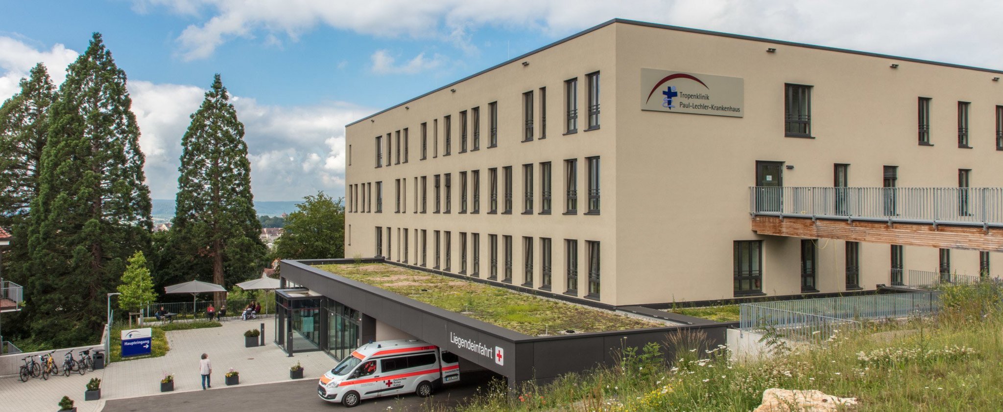 Gebäude der Tropenklinik Paul-Lechler-Krankenhaus mit Vorplatz und Liegendeinfahrt, in der ein Krankenwagen steht.