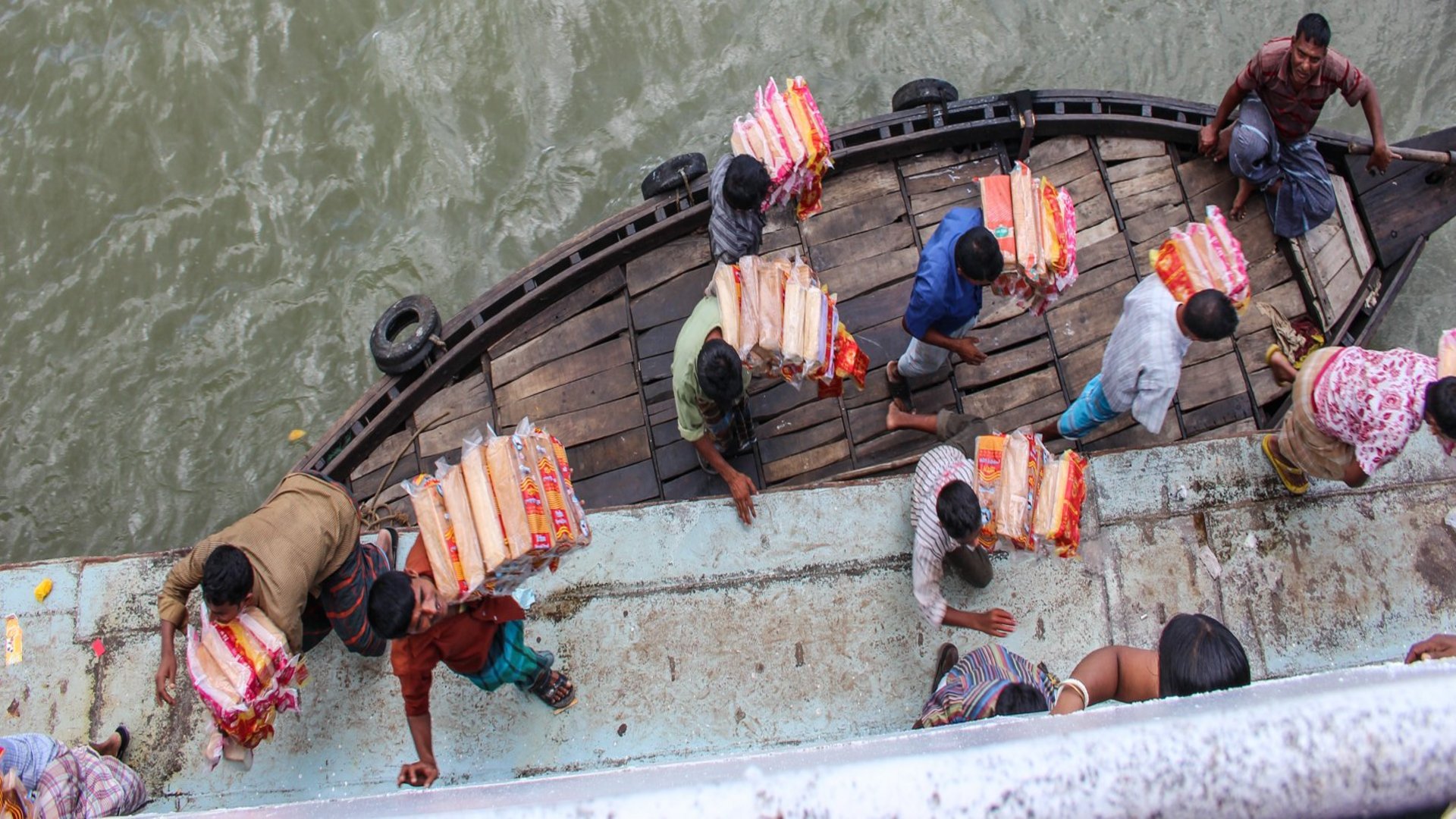 Einige Männer und Frauen tragen Pakete mit Brot von kleinem Holzboot, das an Land angelegt hat.