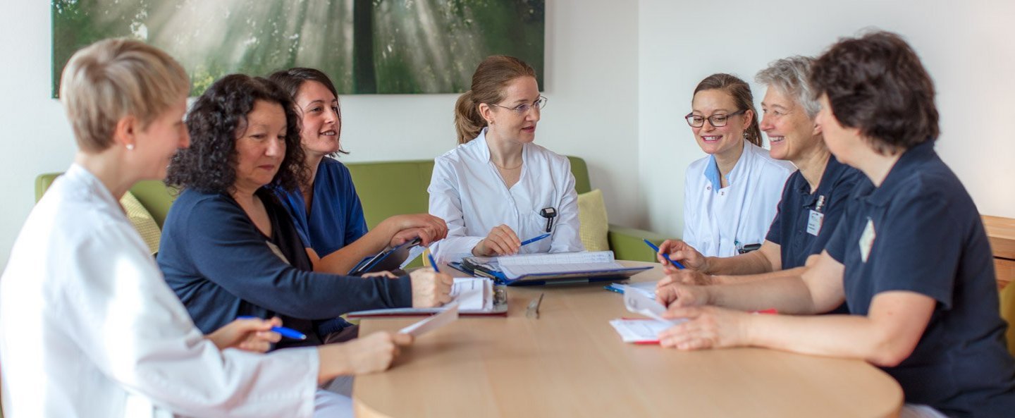 Ärztinnen, Pflegefachfrauen und Mitglieder des interdisziplinären, palliativmedizinischen Teams sitzen um einen Tisch und besprechen sich.