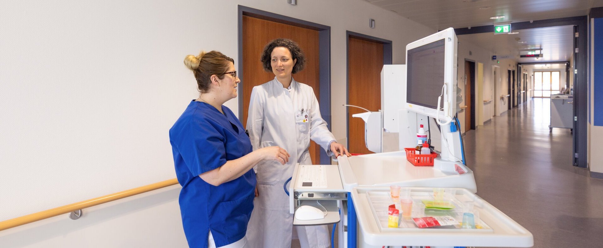 Ärztin und Pflegefachfrau im Gespräch am Patientenwagen.