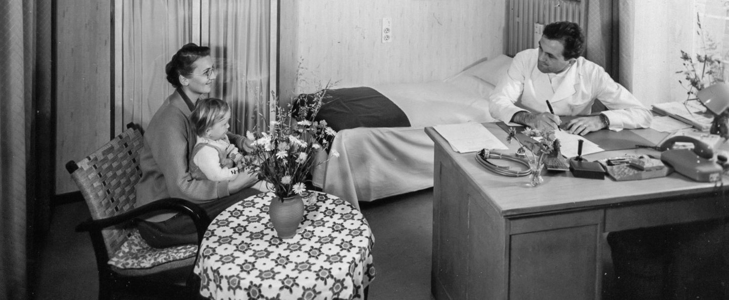 Historisches Bild einer Frau mit Kleinkind im Gespräch mit Arzt im Behandlungszimmer.