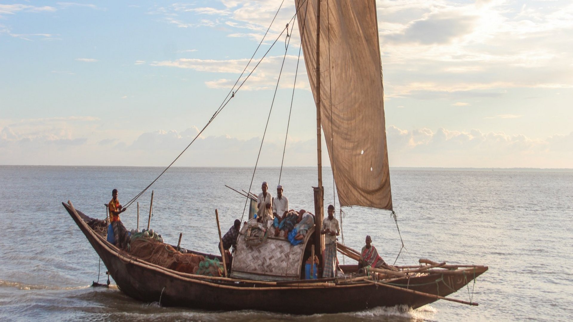 Fischerboot mit gehisstem Seegel und einigen Männern an Bord auf dem Meer.